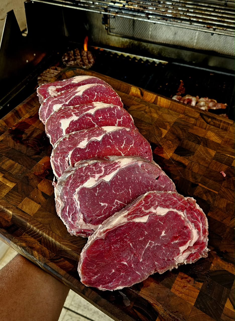 Cortes de carne sobre tábua de madeira em frente à parrilla do FUMASSOU BBQ